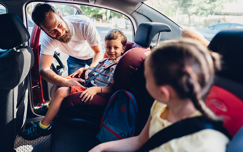 Father buckling his kids into car seats
