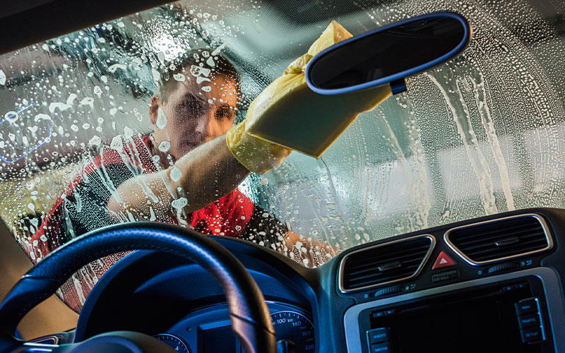 Car wash employee scrubbing windshield