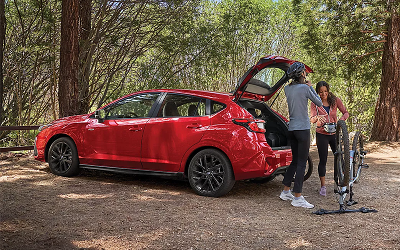 A couple unloading the hatchback of a red 2025 subaru impreza