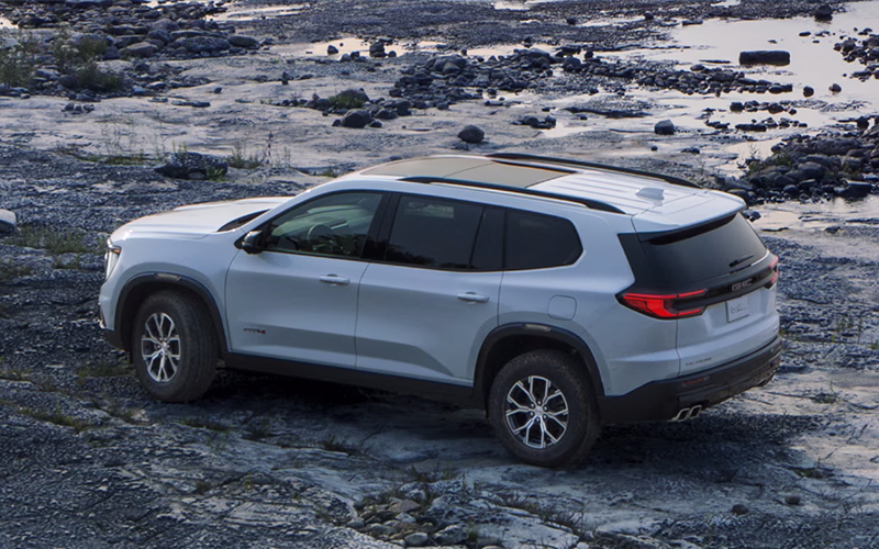 a white 2025 gmc acadia driving in gravel