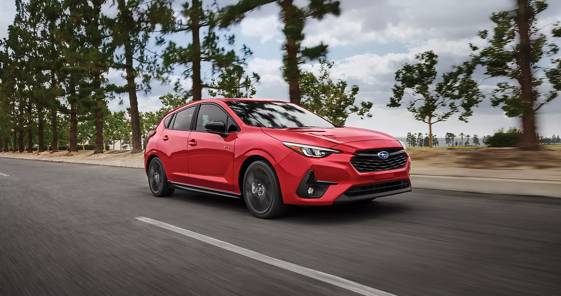 A red 2025 subaru impreza driving past some trees