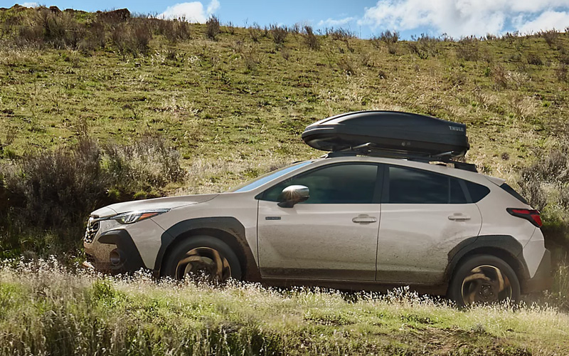 A white 2026 Subaru Crosstrek driving on a dirt road up a hill
