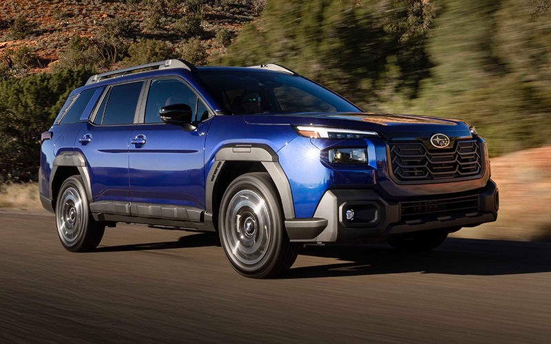 A blue 2026 Subaru Outback driving on a highway in a rural, desert-like setting