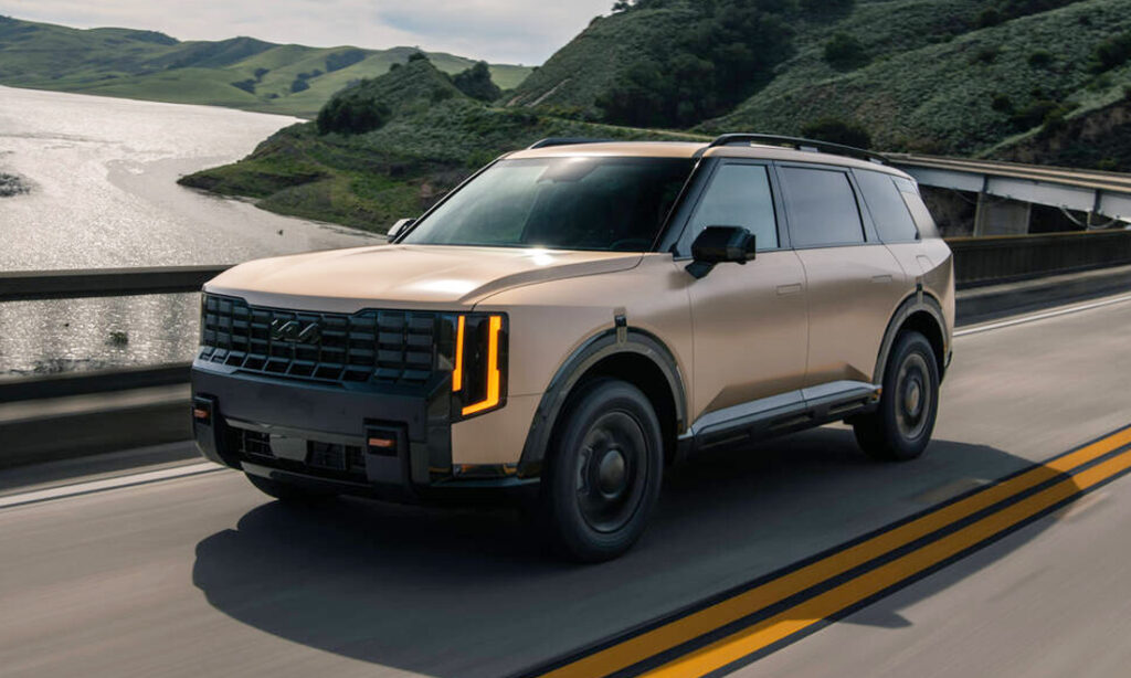 A tan 2027 Kia Telluride in motion on a two-way highway.