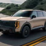 A tan 2027 Kia Telluride in motion on a two-way highway.