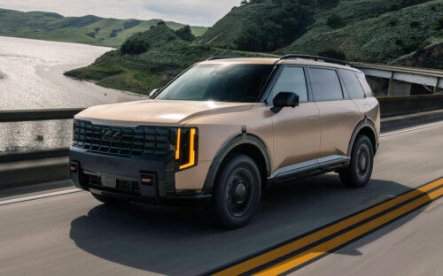 A tan 2027 Kia Telluride in motion on a two-way highway.