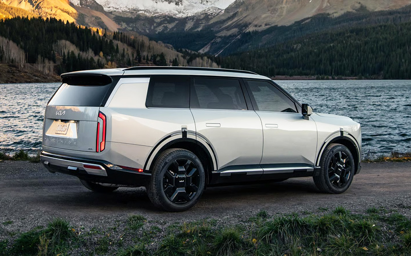 2027 Kia Telluride value A silver 2027 Kia Telluride hybrid parked by a lake in front of a mountain landscape